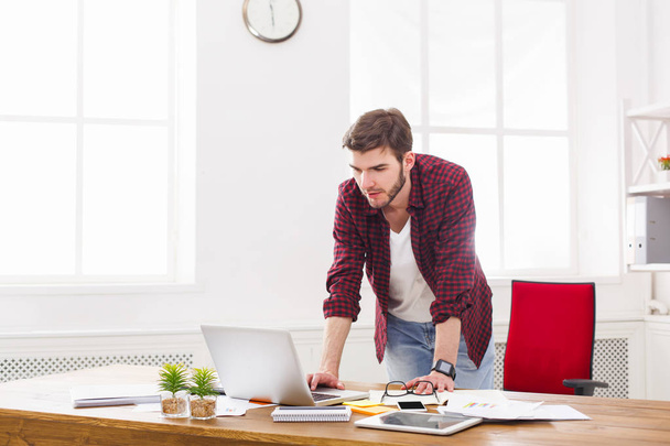 Молодий бізнесмен стоїть біля ноутбука в сучасному білому офісі
 - Фото, зображення