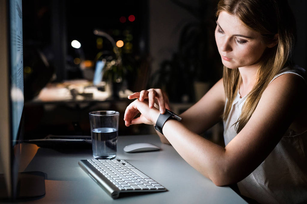 Businesswoman in her office at night looking at watch. - Foto, Imagen