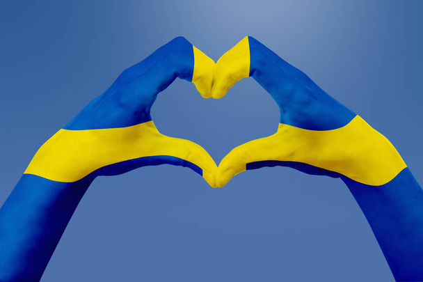 Hands flag of Sweden, shape a heart. Concept of country symbol, on blue sky. - Foto, Imagen