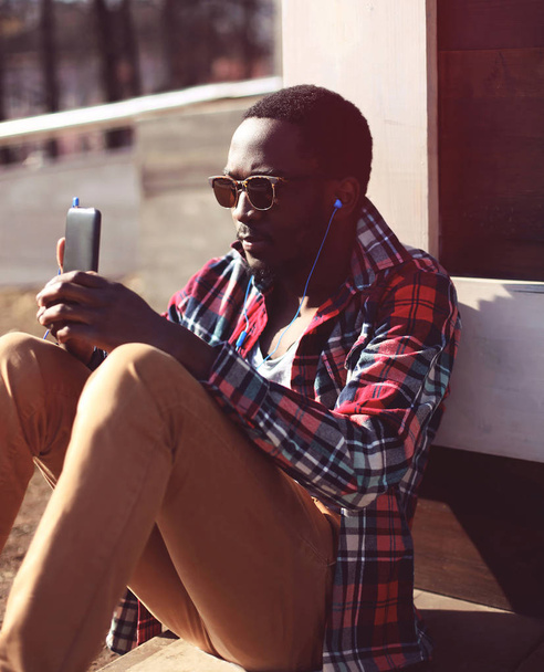 Fashion portrait young african man listens to music using smartp - Фото, изображение