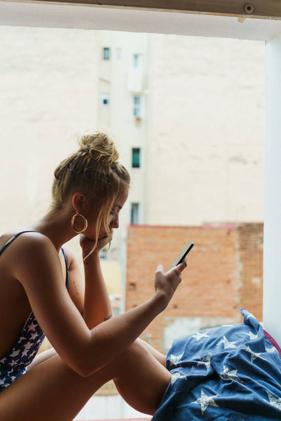Girl browsing phone on window sill - Фото, изображение