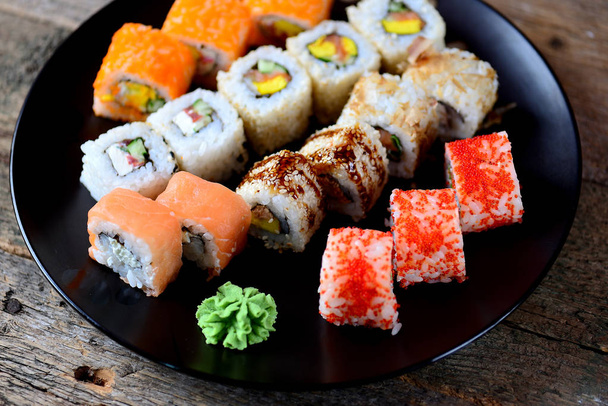 hausgemachtes Sushi mit Lachs, Tobiko-Kaviar, Omelett, Gurke, Sesam und Weichkäse auf altem Holzgrund. rustikaler Stil. - Foto, Bild