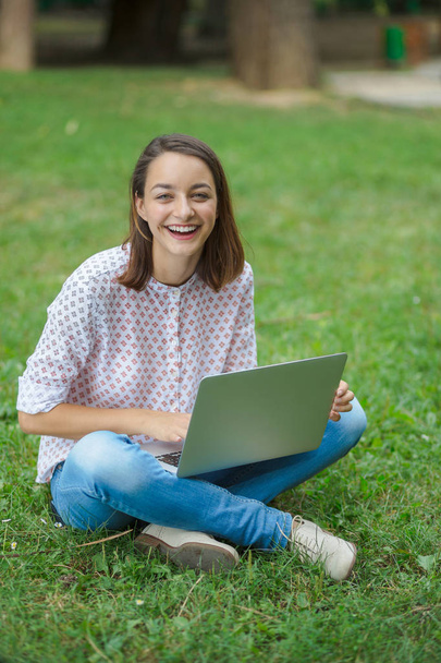 Young woman with laptop sitting on green grass - Foto, Imagen