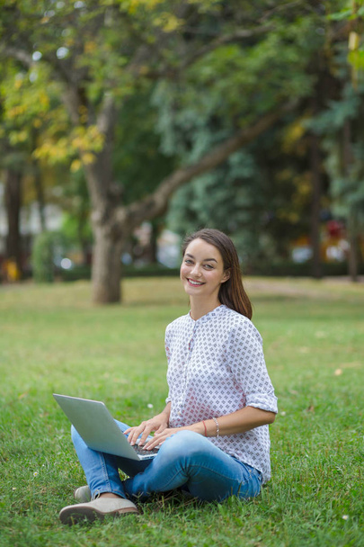 Молодая женщина с ноутбуком сидит на зеленой траве
 - Фото, изображение