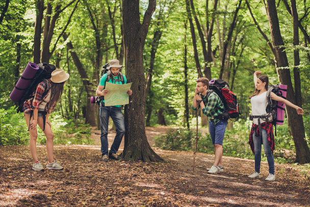 Four tourists stopped for rest in the forest, holding map, tryin - Fotoğraf, Görsel