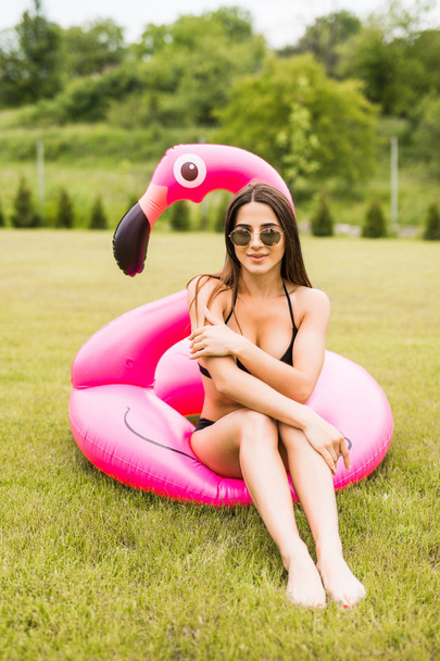Молодая и сексуальная девушка веселится и смеется и веселится на траве возле бассейна на надувном розовом фламинго в купальнике летом
 - Фото, изображение