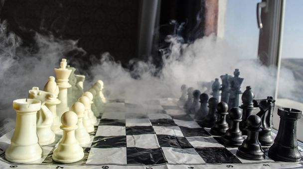 Šachy desková hra koncept podnikatelských nápadů a precizní strategie a soutěž myšlenek. Šachové figury na tmavém pozadí se kouře a mlhy a okno se sluneční světlo. - Fotografie, Obrázek