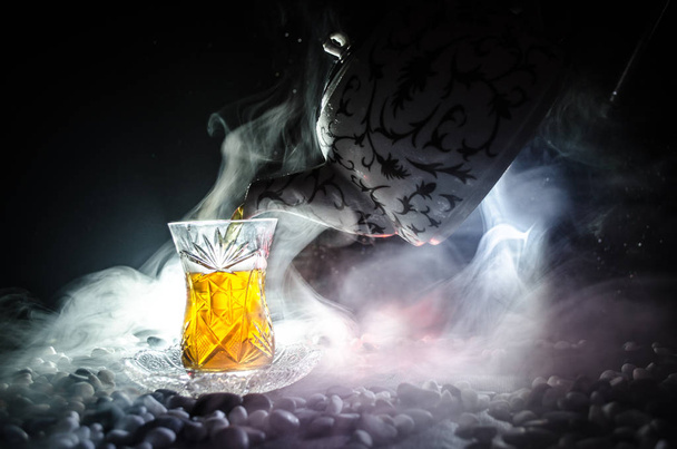 Turkish Azerbaijan tea in traditional glasse and pot on black background with lights and smoke. Armudu traditional cup - 写真・画像