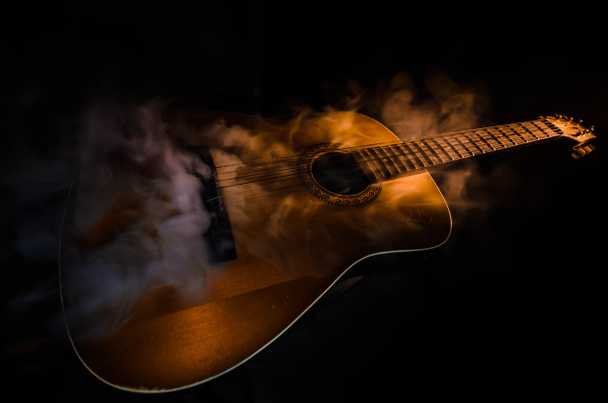 Μουσική αντίληψη. Ακουστική κιθάρα που απομονώνονται σε ένα σκοτεινό φόντο κάτω από την ακτίνα του φωτός με τον καπνό με αντίγραφο χώρο. Χορδές κιθάρας, κοντινό πλάνο. Επιλεκτική εστίαση. Εφέ φωτιά - Φωτογραφία, εικόνα