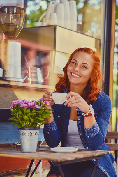 Roodharige vrouw drinkt koffie in een café - Foto, afbeelding