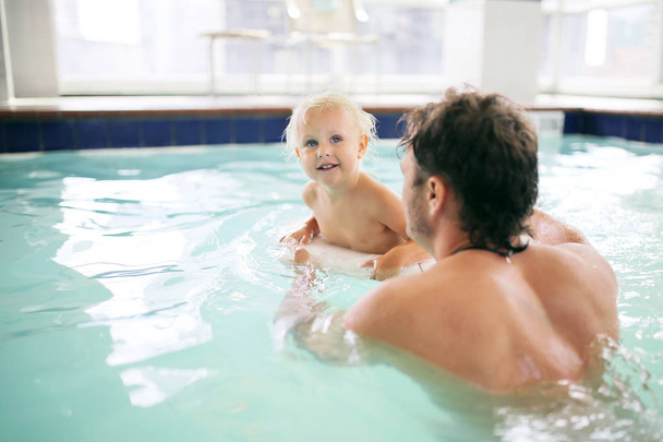 Отец помогает ребенку плавать в закрытом бассейне отеля
 - Фото, изображение