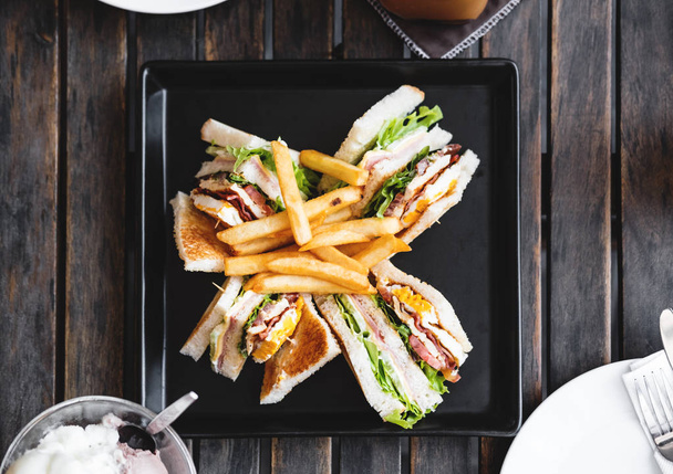 Cuatro rebanadas de sándwiches fritos, sobre plato cuadrado negro, sobre mesa de madera
 - Foto, imagen