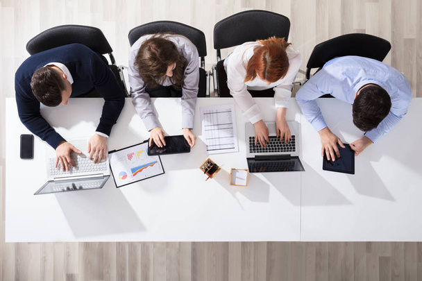 Vista elevada de pessoas de negócios usando dispositivos eletrônicos na mesa no escritório
 - Foto, Imagem