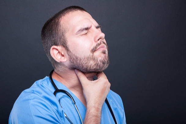 Young doctor wearing scrubs having throat pain - Фото, изображение
