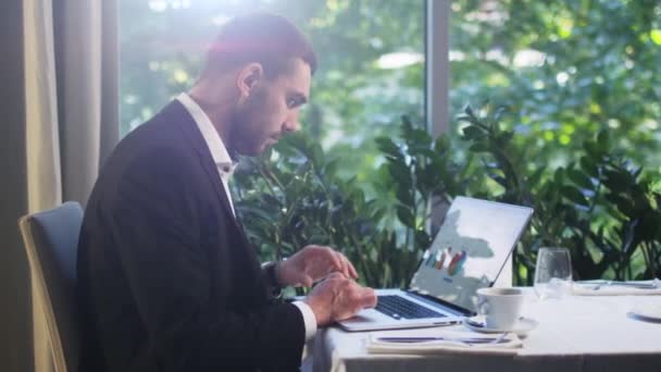 Businessman in a suit is working on laptop and drinking coffee at a restaurant. - Metraje, vídeo