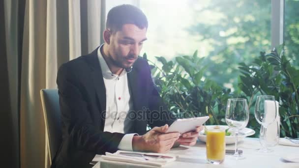 Businessman in a suit is happy to see successful results on a tablet in a restaurant. - Metraje, vídeo