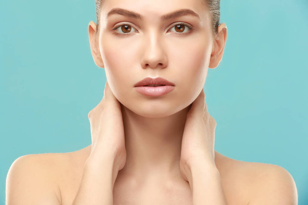 Closeup view of beautiful young woman with natural lips makeup touching neck on color background - Φωτογραφία, εικόνα