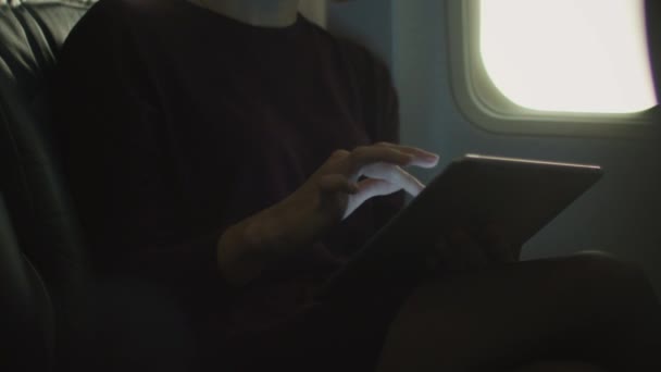 Young woman in close-up is using a tablet inside an airplane next to a window. - Πλάνα, βίντεο