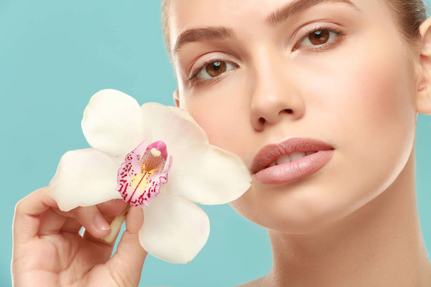 Closeup view of beautiful young woman with natural lips makeup and flower on color background - Valokuva, kuva