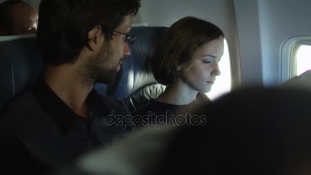 Young woman is working on a laptop inside an airplane next to a window while a man talks to her. - Filmati, video