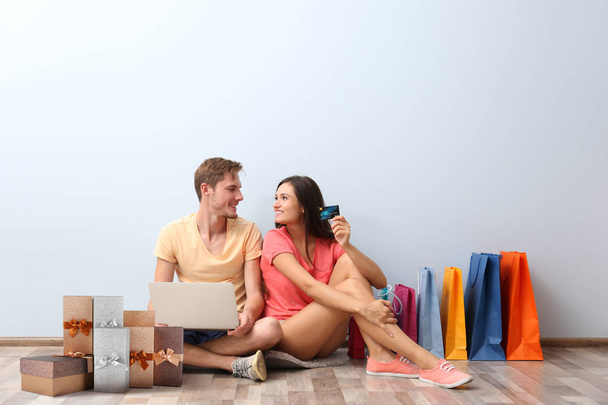 Internet shopping concept. Young couple sitting with laptop and purchases near wall at home - Фото, изображение
