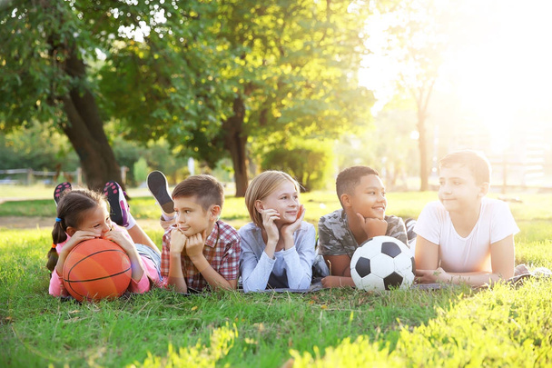 Cute children with sport balls lying on green grass at park, Football and basketball concept - Φωτογραφία, εικόνα