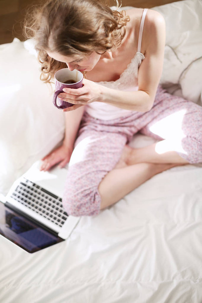 Young beautiful woman sitting in bed with laptop. - Foto, afbeelding