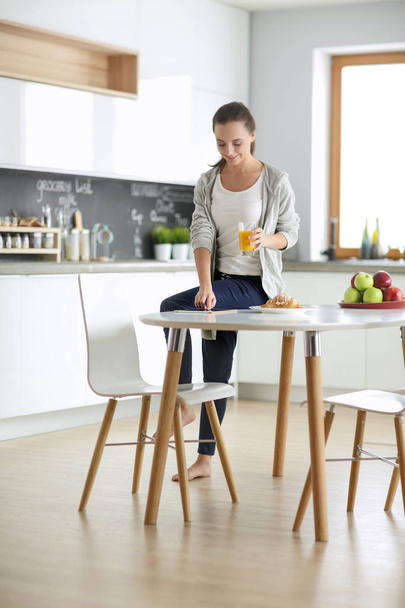 Young woman with orange juice and tablet in kitchen. - Foto, Bild