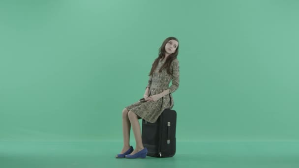 a young woman is sitting on the black luggage and waiting - Materiał filmowy, wideo