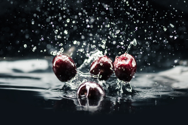 ripe cherries falling in water - Foto, afbeelding