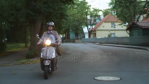 Young man in an elegant beige trench coat rides a retro scooter in a rural residential area. - Footage, Video