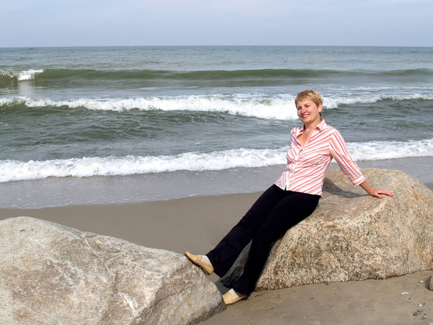 The woman of average years sits on a boulder. Coast of the Baltic Sea - Φωτογραφία, εικόνα