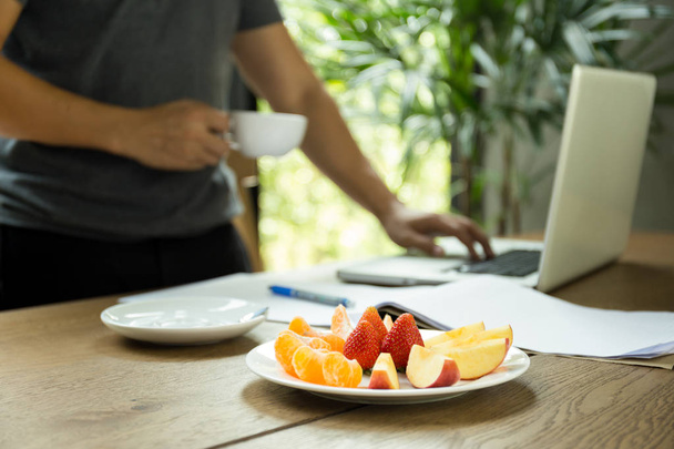 Enfoque seleccionado fruta fresca con el hombre sosteniendo la taza de café workin
 - Foto, imagen