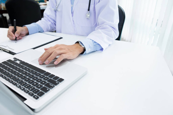 Médecin travaillant avec un ordinateur portable et écrivant sur la paperasse
 - Photo, image