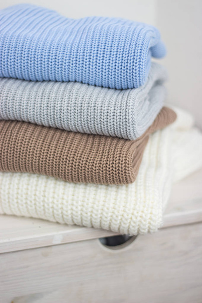A pile of warm autumn clothing on a wooden shelf. Sweaters. Knitted winter wear. Cozy. - Fotó, kép