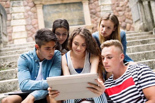 Teenage students with tablet sitting on stone steps. - Zdjęcie, obraz