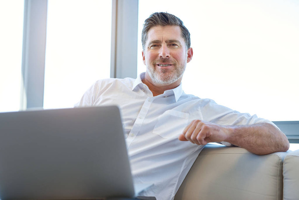 Portrait of a mature businessman sitting comfortably with a laptop computer on his lap, smiling positively at the camera - Foto, Imagen