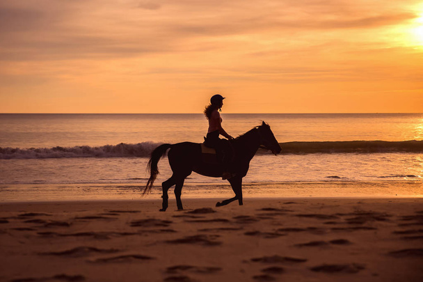 σιλουέτα του αναβάτη θηλυκό άλογο cantering στην αμμώδη παραλία στο ηλιοβασίλεμα - Φωτογραφία, εικόνα