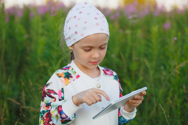 kleines blondes Mädchen mit digitalem Tablet in der Natur - Foto, Bild