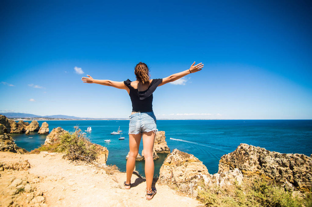 schöne lateinische Frau steht auf einem Felsen über dem Ozean und begrüßt den Sommer - Foto, Bild