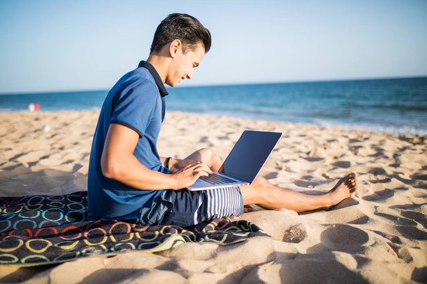 Nuori aasialainen mies työskentelee kannettavan tietokoneen kanssa trooppisella rannalla
  - Valokuva, kuva