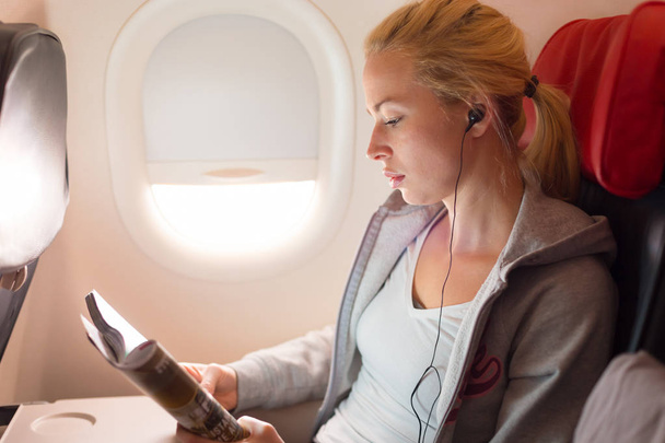 Magazynu Woman czytanie i słuchanie muzyki na samolot. - Zdjęcie, obraz