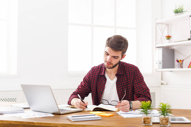 Jovem empresário concentrado toma notas no escritório branco moderno
 - Foto, Imagem
