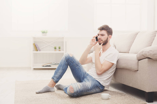Zamyšlený mladý muž doma mluví na mobil - Fotografie, Obrázek