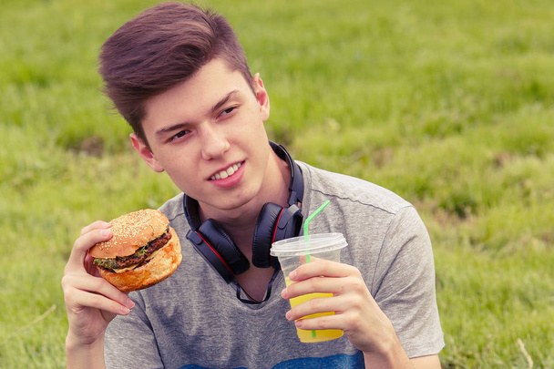 fiatal srác pihen, és eszik egy hamburgert, naplementekor - Fotó, kép