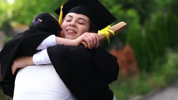 Buiten scène van mooie vrouwelijke afstuderen student gekleed in de cup en jurk, haar ouders knuffelen. - Video