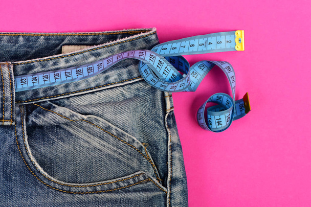 Denim trousers and measure tape isolated on pink background - Foto, afbeelding