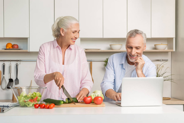 Mature loving couple family using laptop and cooking salad - Valokuva, kuva