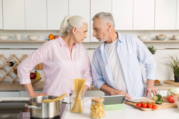 Angry mature man standing near mature serious woman at kitchen - Foto, afbeelding