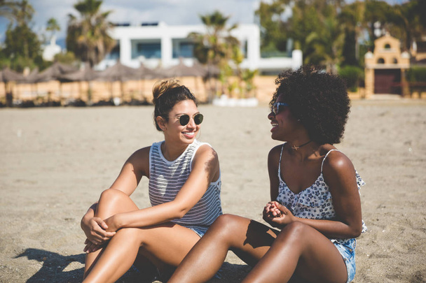 Two pretty girls sitting on beach talking - Photo, image